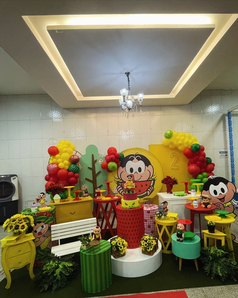 Cenário da Turma da Mônica com painel, banco de jardim, girassóis e balões coloridos